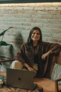 Woman working on a laptop at home, seated on a sofa with a warm ambiance.